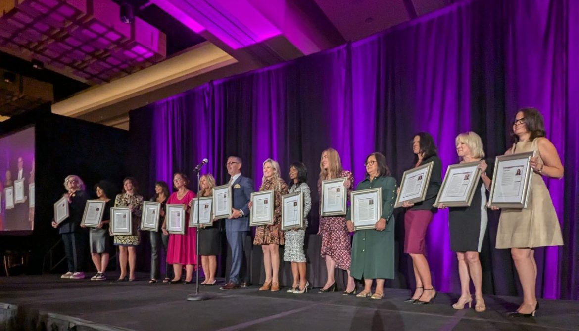 The full class of Women of Achievement honorees lined up on stage holding their framed certificates.
