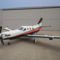 A white and red Daher TBM 910 turboprop parked on the ramp in front of a hangar