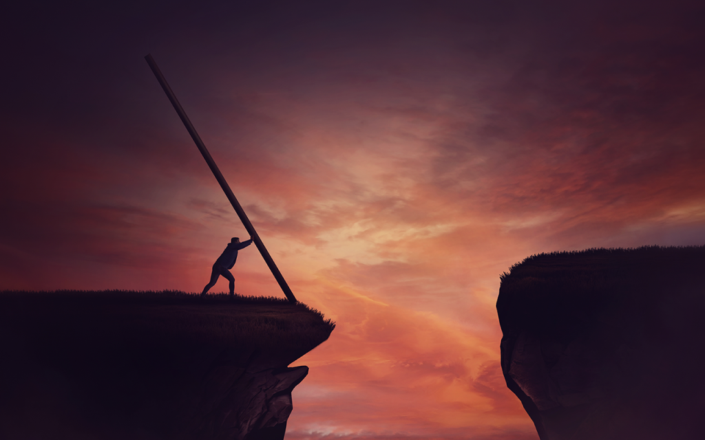 Silhouetted figure at a cliff edge at sunset using a long pole to bridge a gap