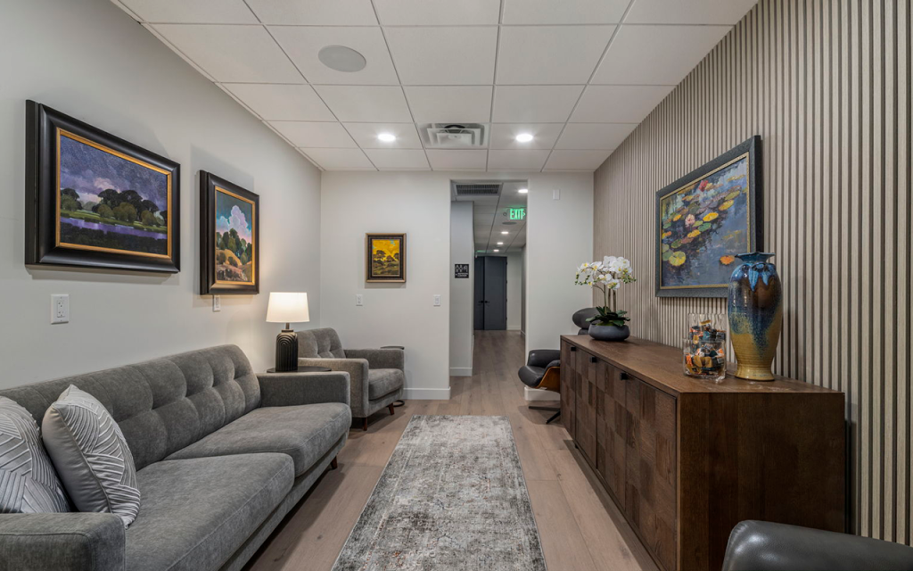 Therapy room with a gray sofa, framed artwork and a console table at Redefine Wellness & Treatment
