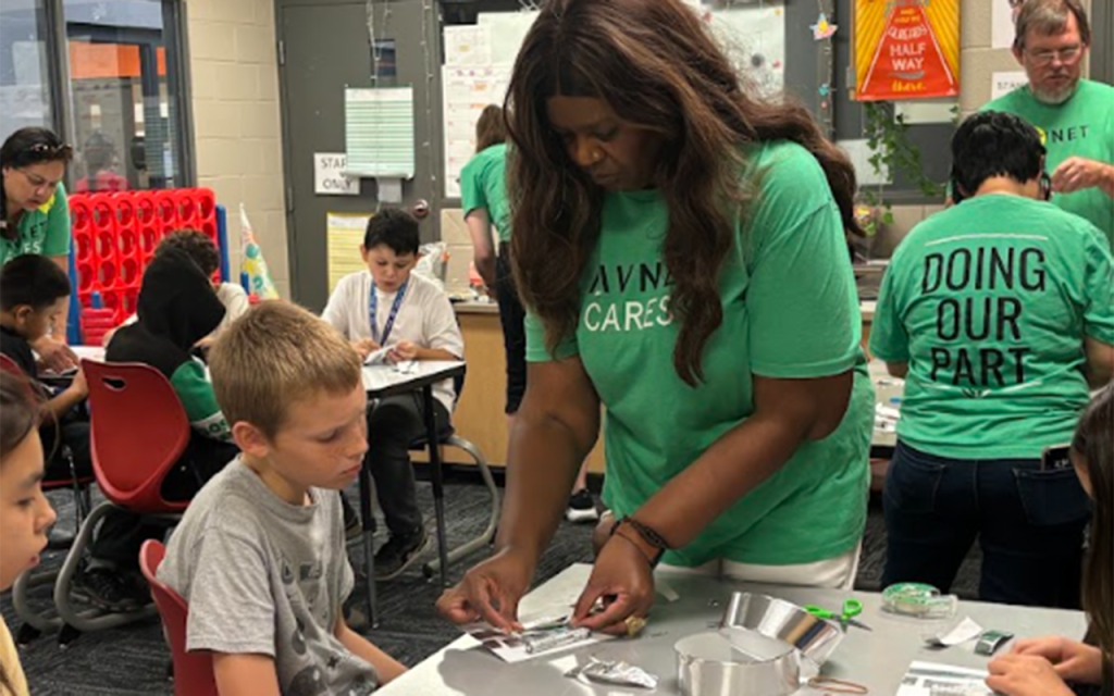 Children and a volunteer in a green T-shirt working on a hands-on STEM activity